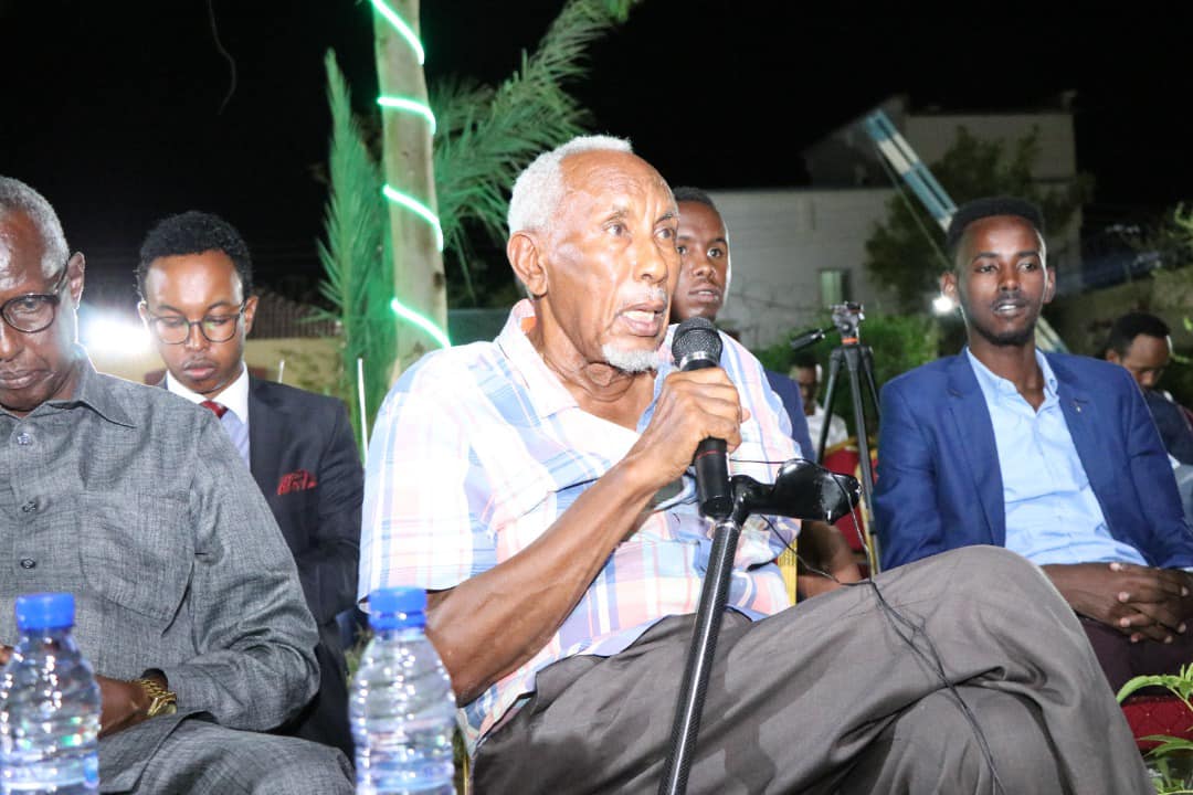 A community elder speaking into a microphone from the audience during the public forum